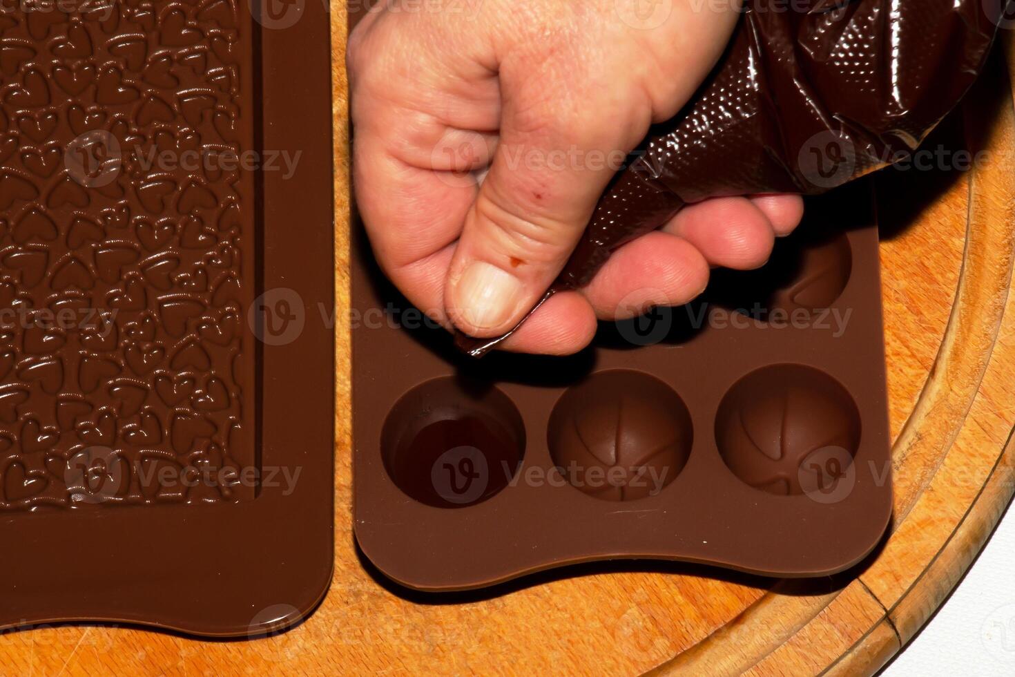 The chef's hands pour hot chocolate into silicone molds using cooking envelopes. photo