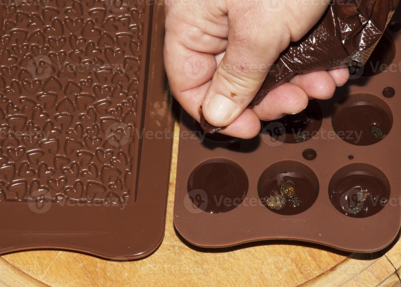 The chef's hands pour hot chocolate into silicone molds using cooking envelopes. photo