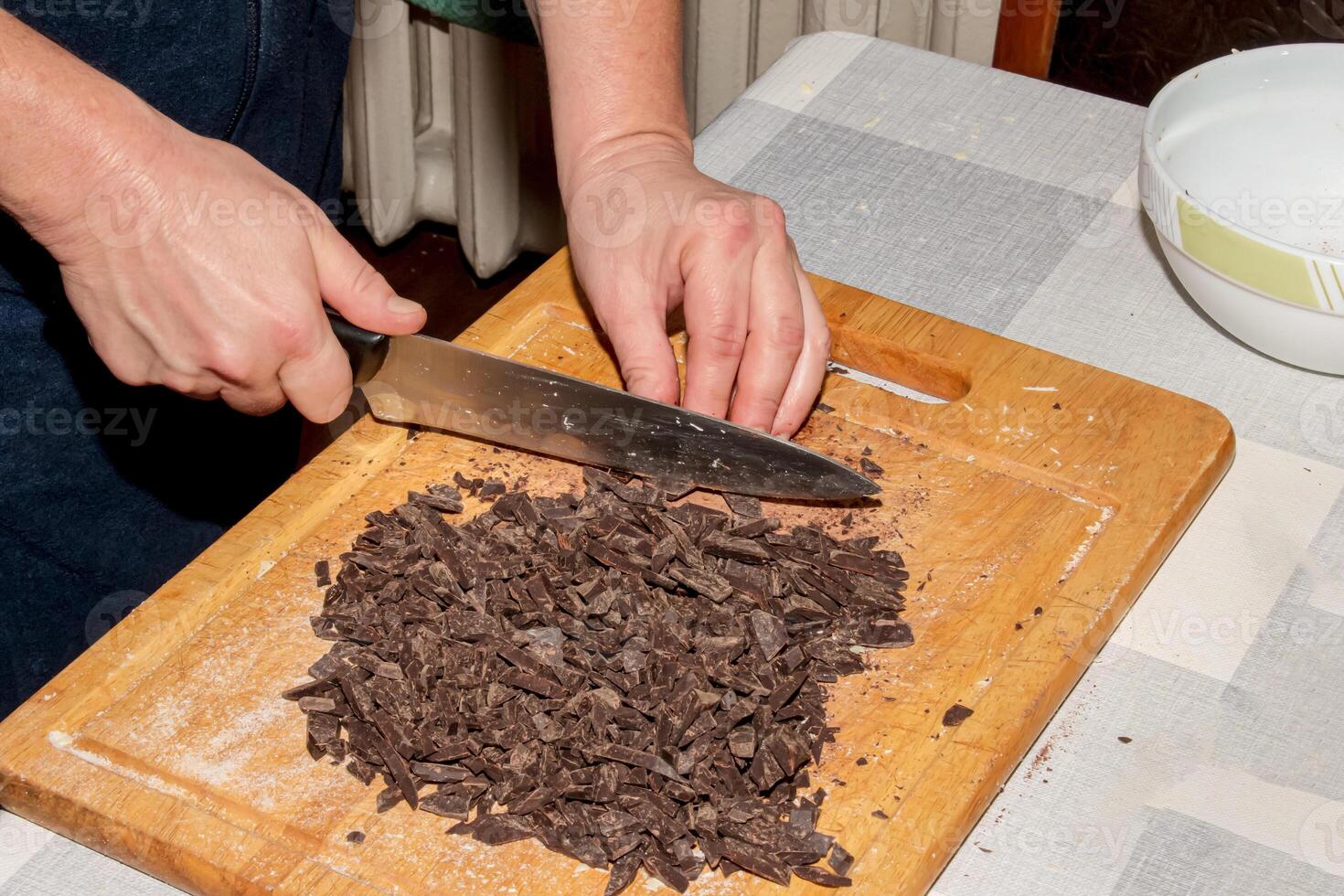The hands of the cook crush the grated cocoa with a knife on a wooden kitchen board to make chocolate. photo