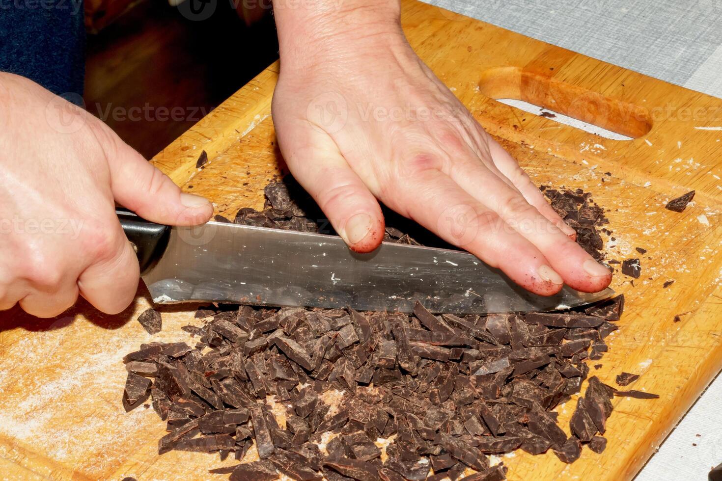 The hands of the cook crush the grated cocoa with a knife on a wooden kitchen board to make chocolate. photo
