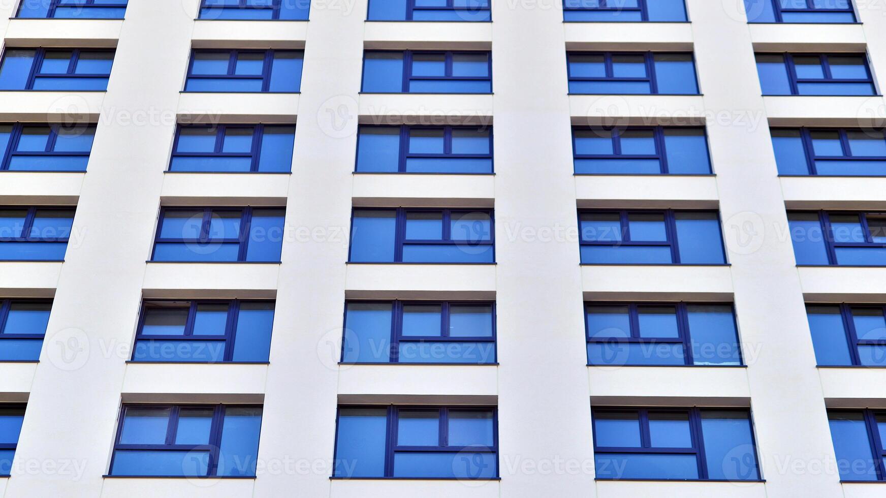 Modern high-rise apartment building in white, stand tall against a blue sky, exemplifying innovative urban architecture with sleek, angular designs. photo