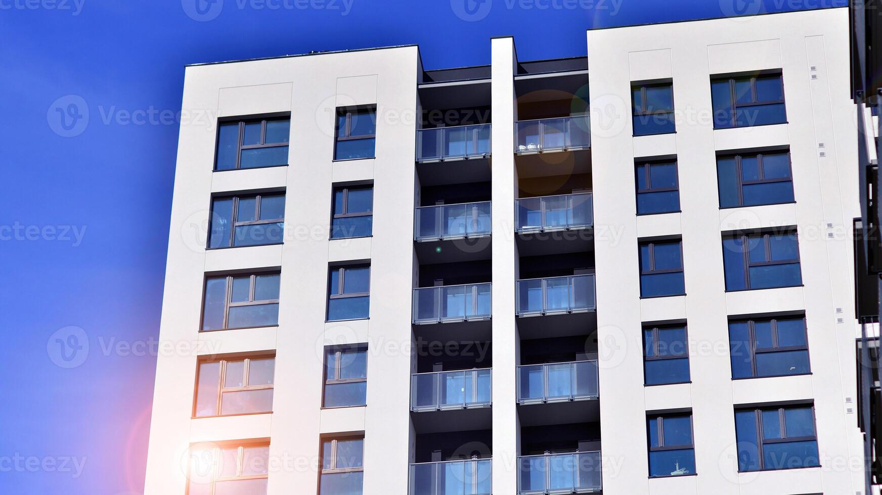 Modern high-rise apartment building in white, stand tall against a blue sky, exemplifying innovative urban architecture with sleek, angular designs. photo