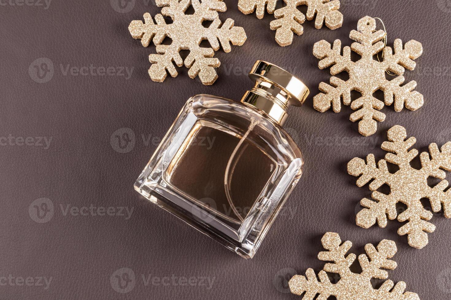 Chic bottle of perfume with a gold cap on a brown leather with Christmas golden snowflakes. An empty mockup of a non branded bottle. top view. photo