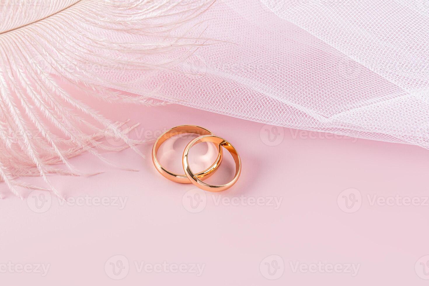 Two classic gold rings on a pink background with part of a white bridal veil with a delicate airy feather. A copy space. design, postcard, invitation. photo