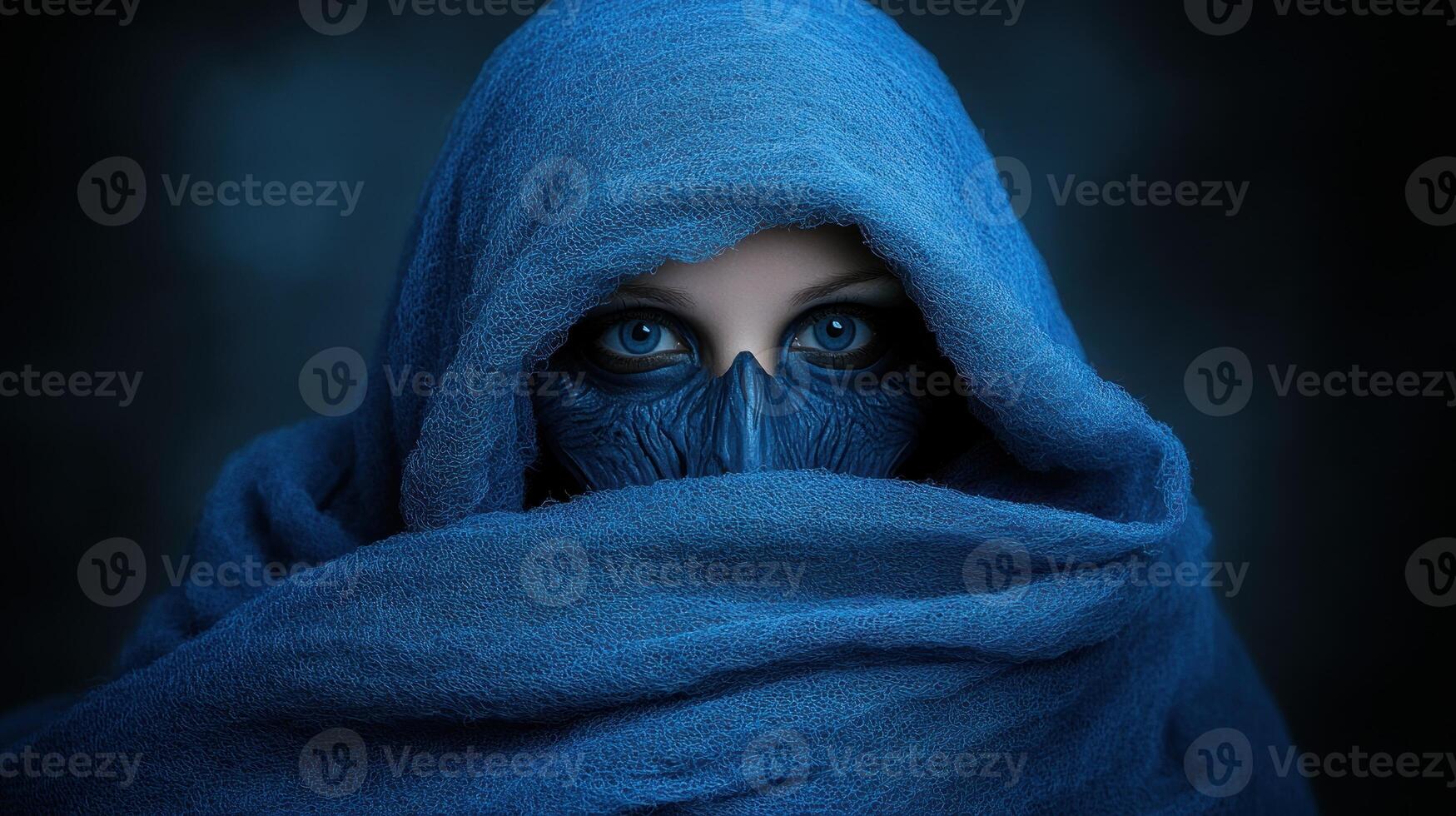 A captivating figure shrouded in blue fabric with striking eyes peering out intensely photo