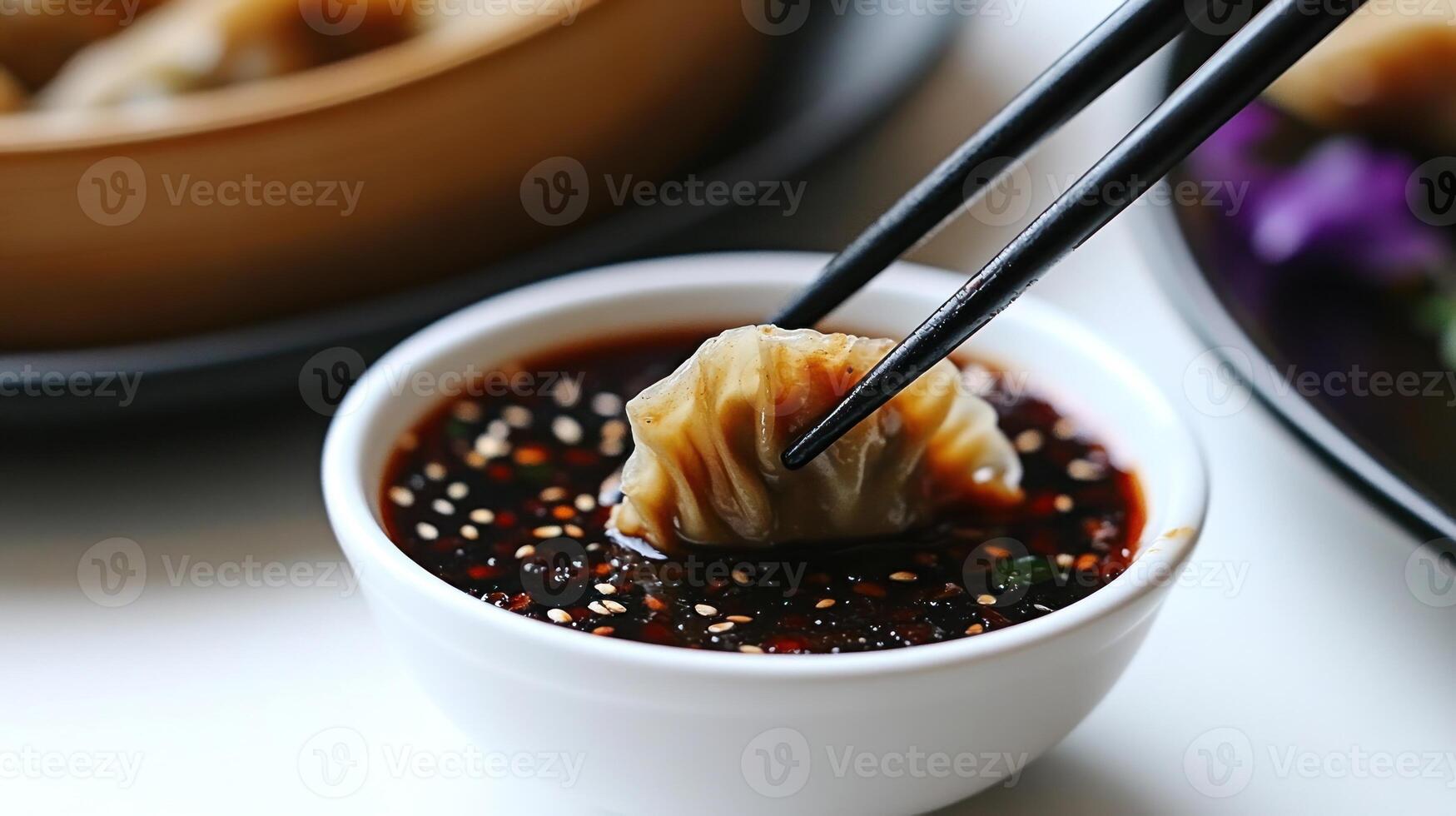 A dumpling is being dipped into a flavorful soy sauce blend with sesame seeds photo