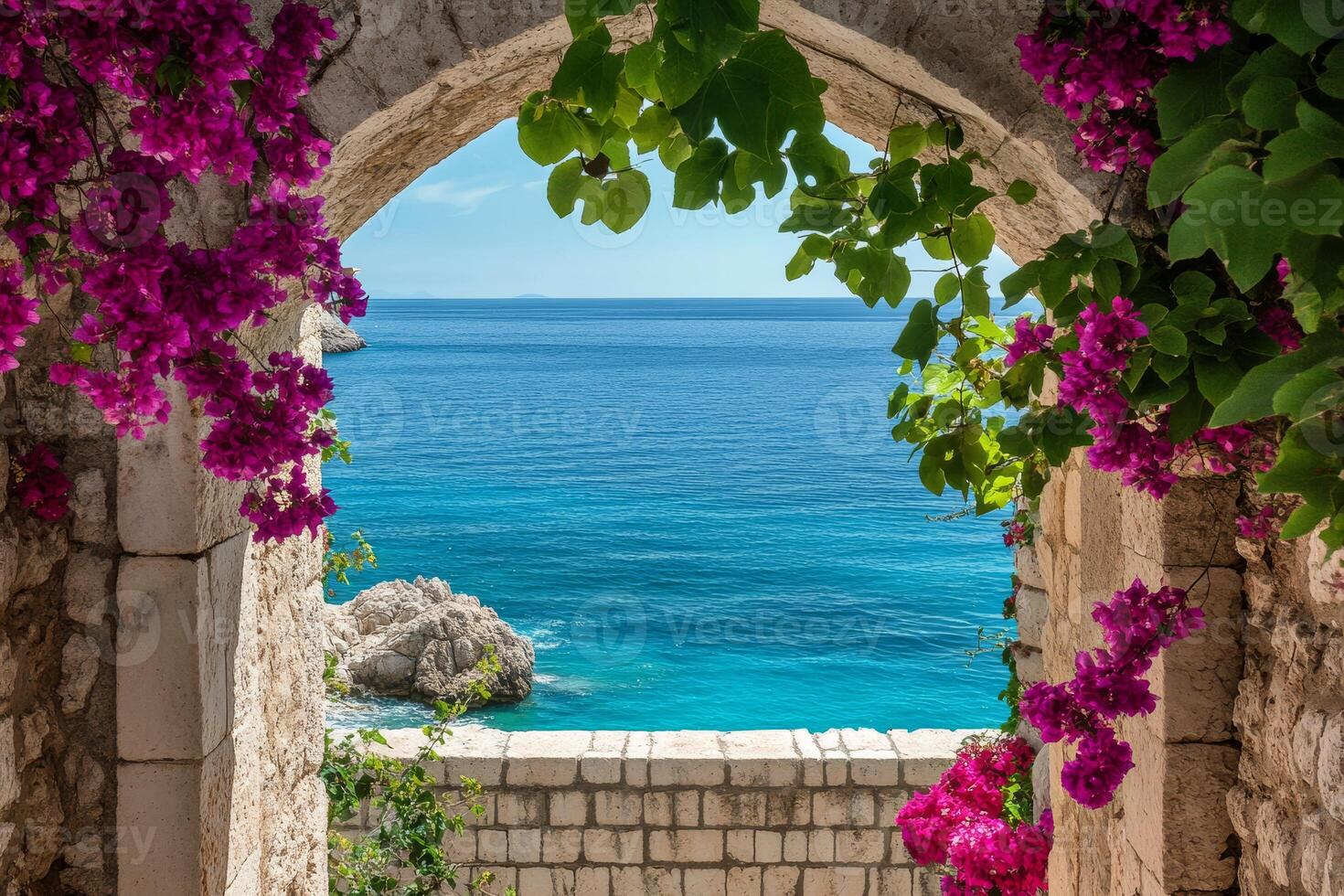 A truly picturesque arch, beautifully adorned with vibrant pink flowers, frames a stunning view of the serene blue sea beyond, blending natural beauty with remarkable architectural charm photo