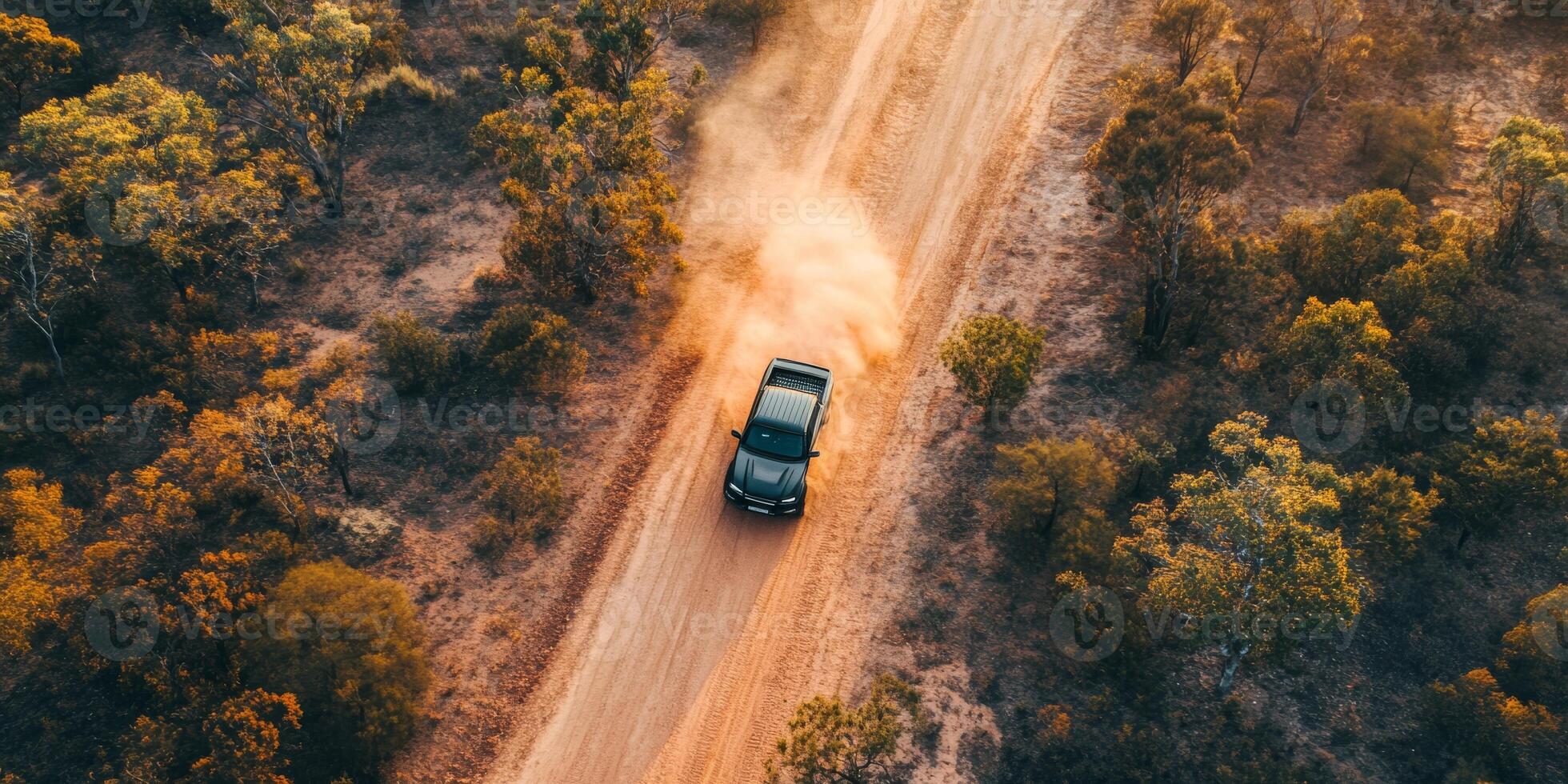 A rugged black pickup truck steadily drives along a winding dirt road, which is surrounded by vibrant and lush greenery, kicking up a trail of dust in a truly picturesque outdoor scene photo