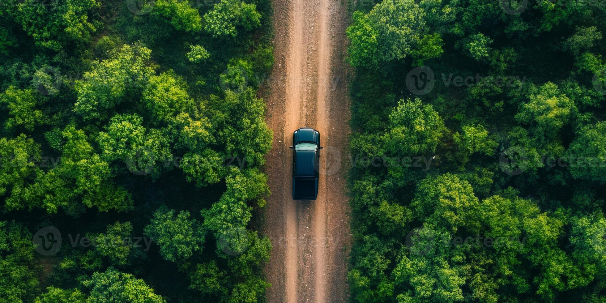 An aerial shot captures a sleek black pickup truck as it skillfully navigates a winding dirt road that snakes through a dense and vibrant forest, sending up a trail of dust behind it with each move photo