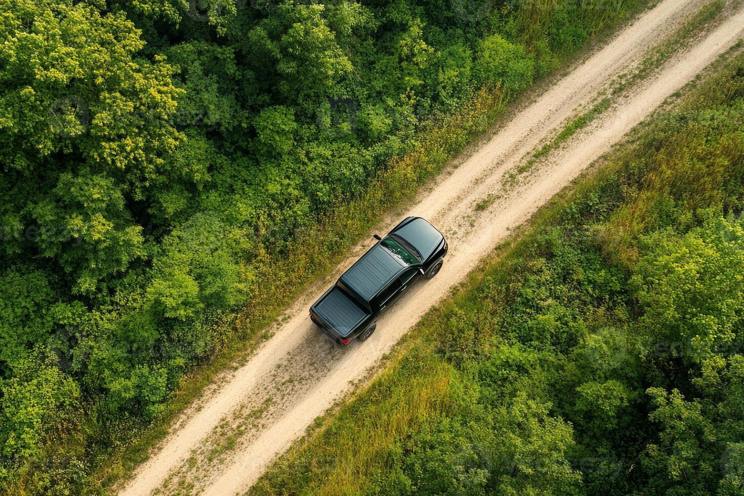 An aerial shot shows a rugged black pickup truck navigating a winding dirt road through a vibrant forest, kicking up dust as it accelerates, highlighting the thrill of exploration photo
