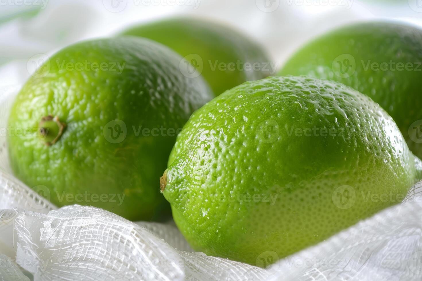 Close-up of four fresh green limes placed on a white cloth background, highlighting their vibrant color. photo