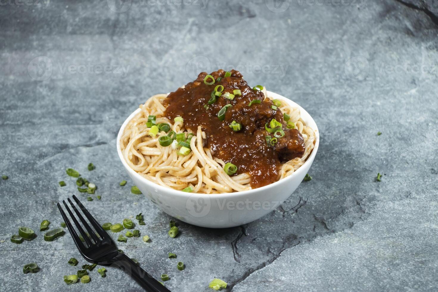 Kam heong chicken noodles with green onion and fork served in bowl isolated on grey background side view of asian food photo