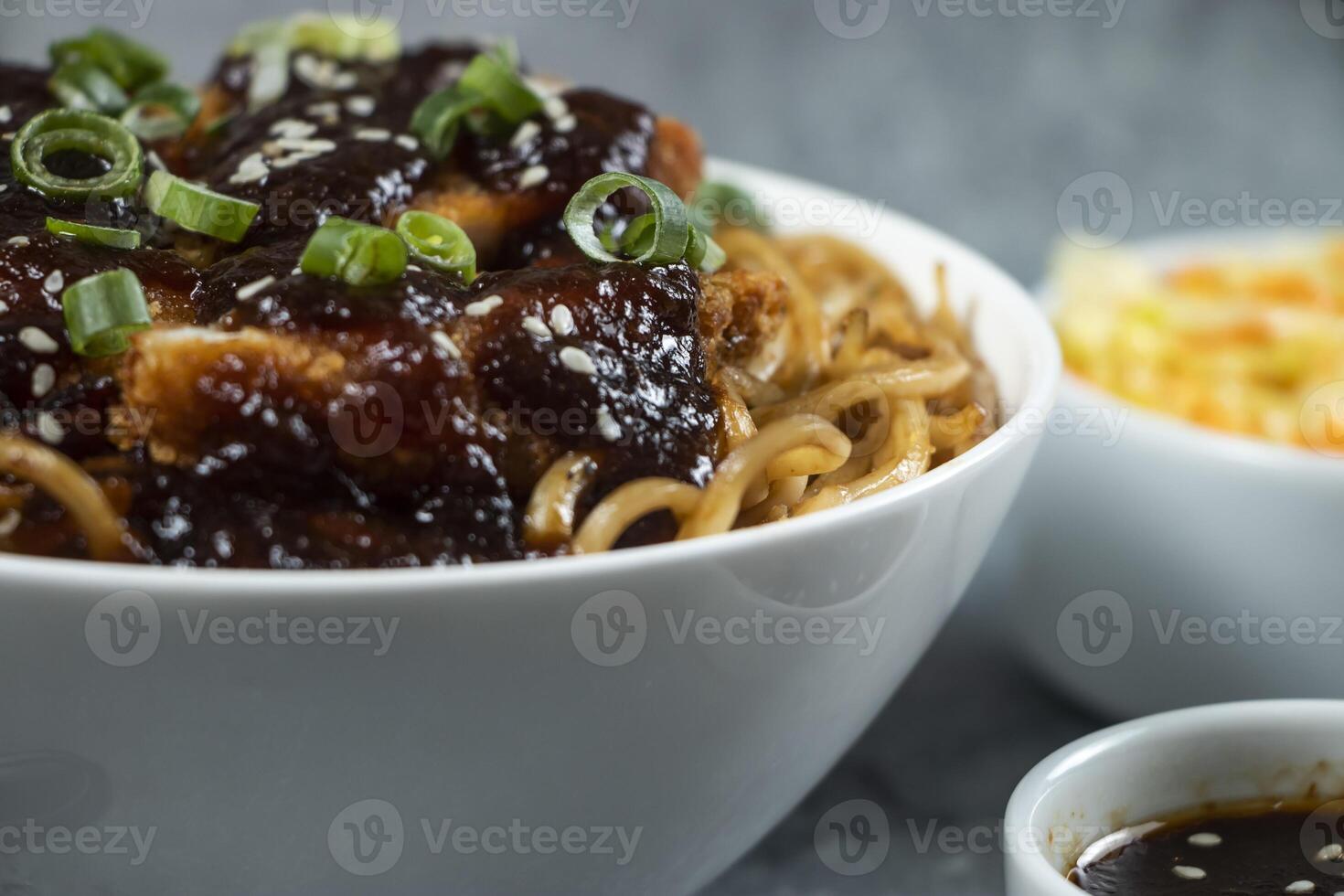 Spicy Teriyaki Fried Chicken Noodles with green onion, spicy sauce, cabbage salad and fork served in bowl isolated on grey background side view of japanese food photo