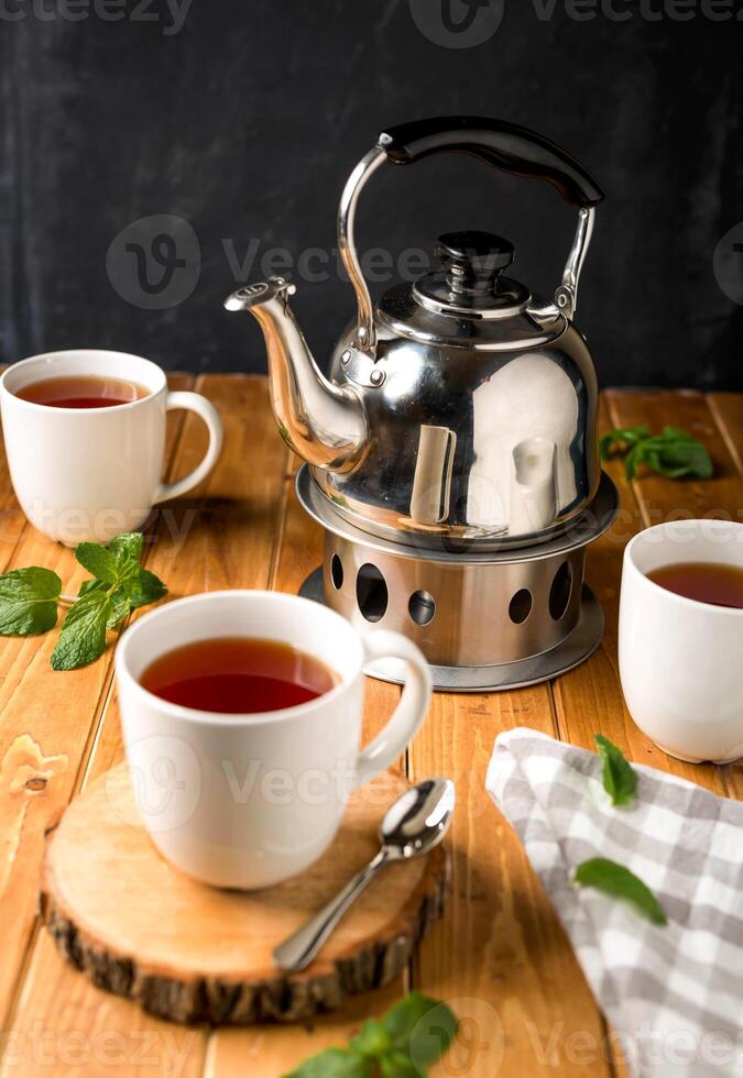 English Breakfast tea served in cups with teapot and mint leaves isolated on wooden table side view of hot tea photo