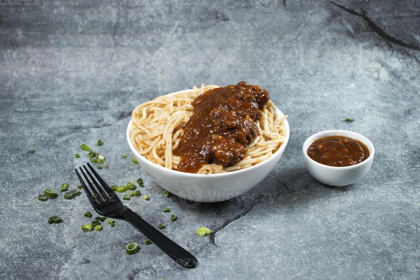 Kam heong chicken noodles with Spicy sauce, green onion and fork served in bowl isolated on grey background side view of asian food photo