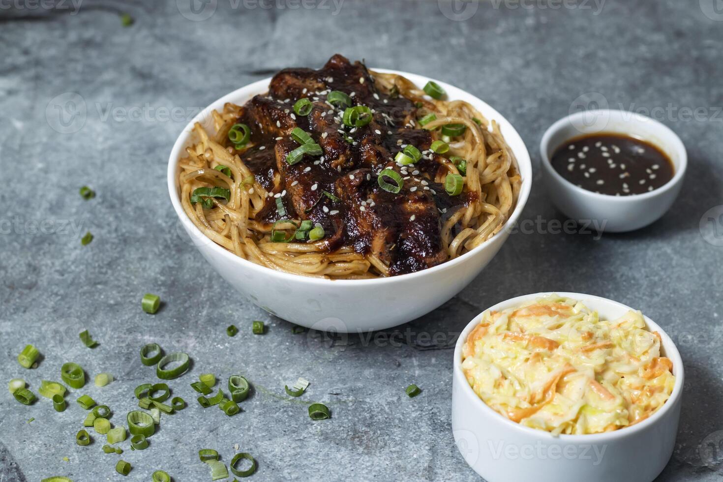 Teriyaki Grilled Chicken Noodles with green onion, spicy sauce, cabbage salad and fork served in bowl isolated on grey background closeup side view of asian food photo