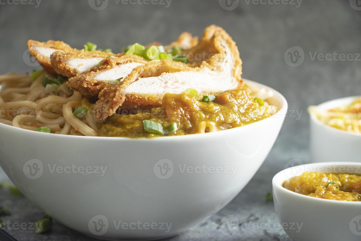 Katsu Chicken Noodles with potato curry, cabbage salad, green onion and fork served in bowl isolated on grey background closeup side view of Asian food photo
