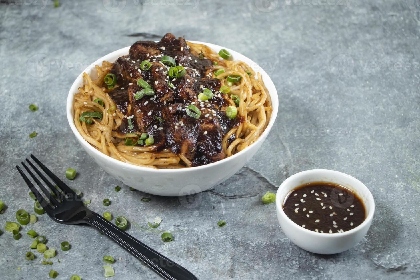 Teriyaki Grilled Chicken Noodles with green onion, spicy sauce and fork served in bowl isolated on grey background side view of japanese food photo