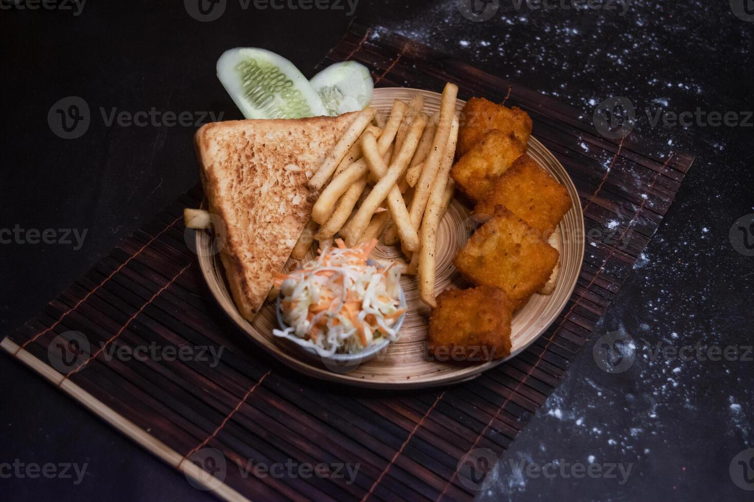 Chicken Nuggets with tomato, onion, lettuce leave, capsicum, french fries and salad served in wooden plate isolated on dark background side view of bangladeshi fast food photo