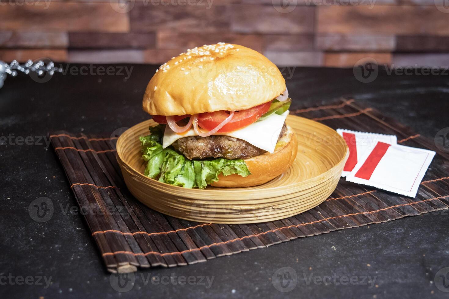 Beef Cheese Burger include tomato, onion, lettuce leave and capsicum served in wooden plate isolated on dark background side view of bangladeshi fast food photo