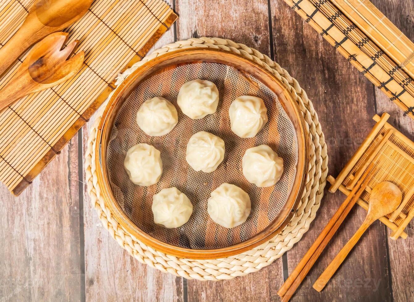 Fresh Steamed meat soup dumplings with chopsticks and spoon served in bamboo steamer isolated on wooden table top view of taiwan food photo