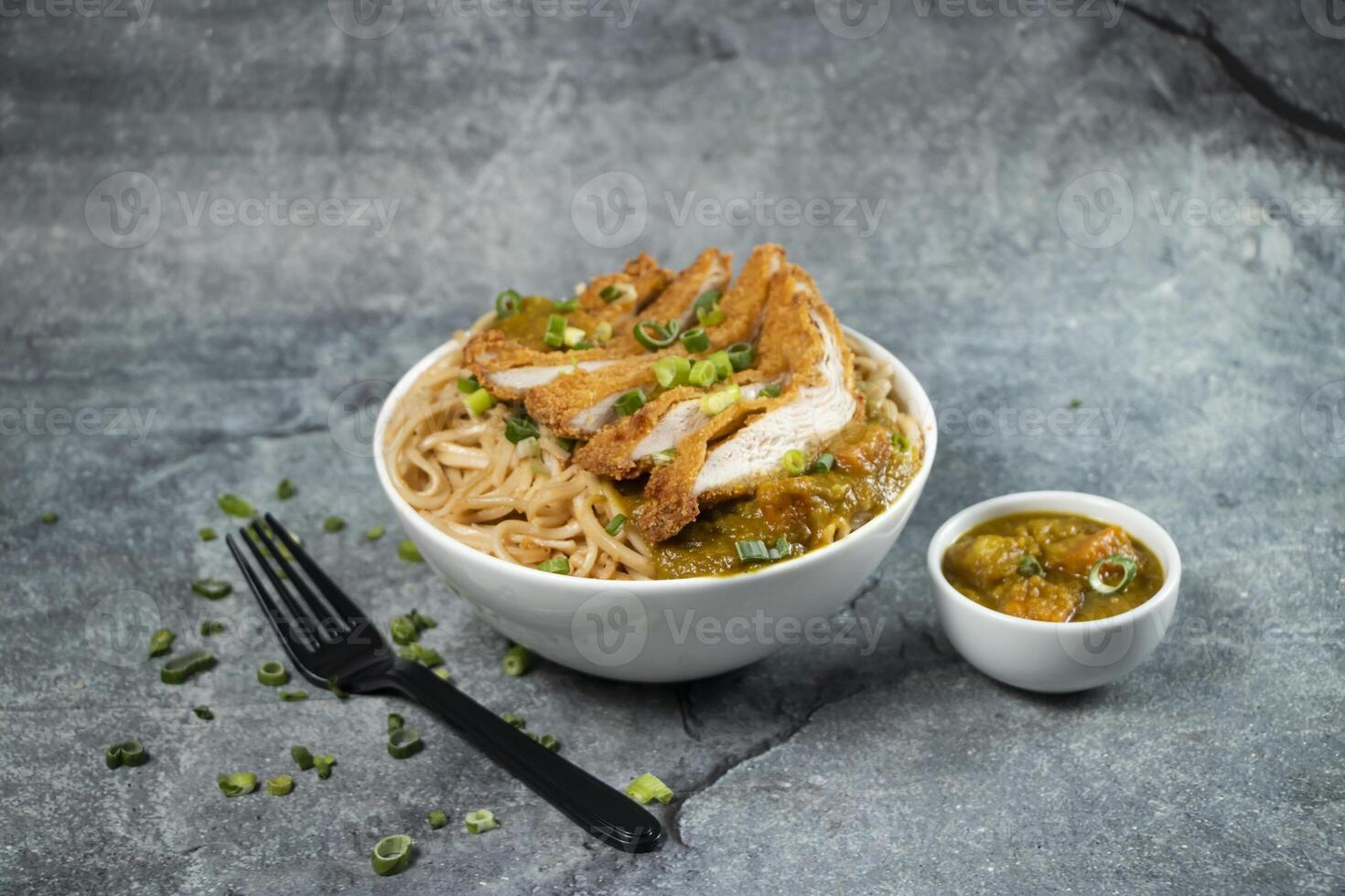 Katsu Chicken Noodles with potato curry, green onion and fork served in bowl isolated on grey background side view of asian food photo