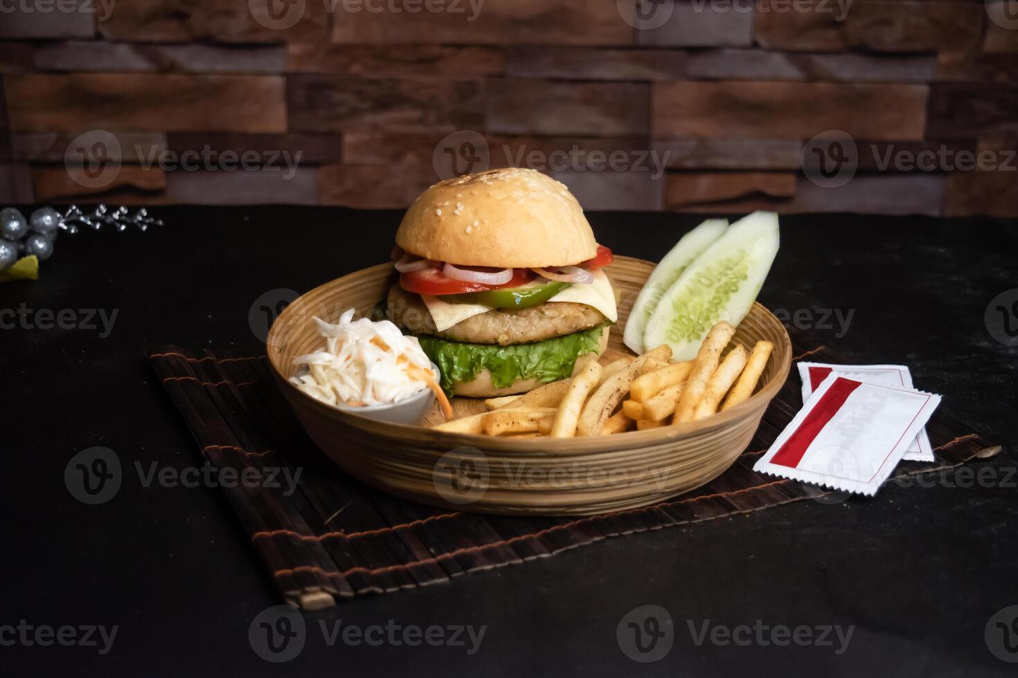 Chicken cheese burger basket include tomato, onion, lettuce leave, capsicum, french fries and salad served in wooden plate isolated on dark background side view of bangladeshi fast food photo