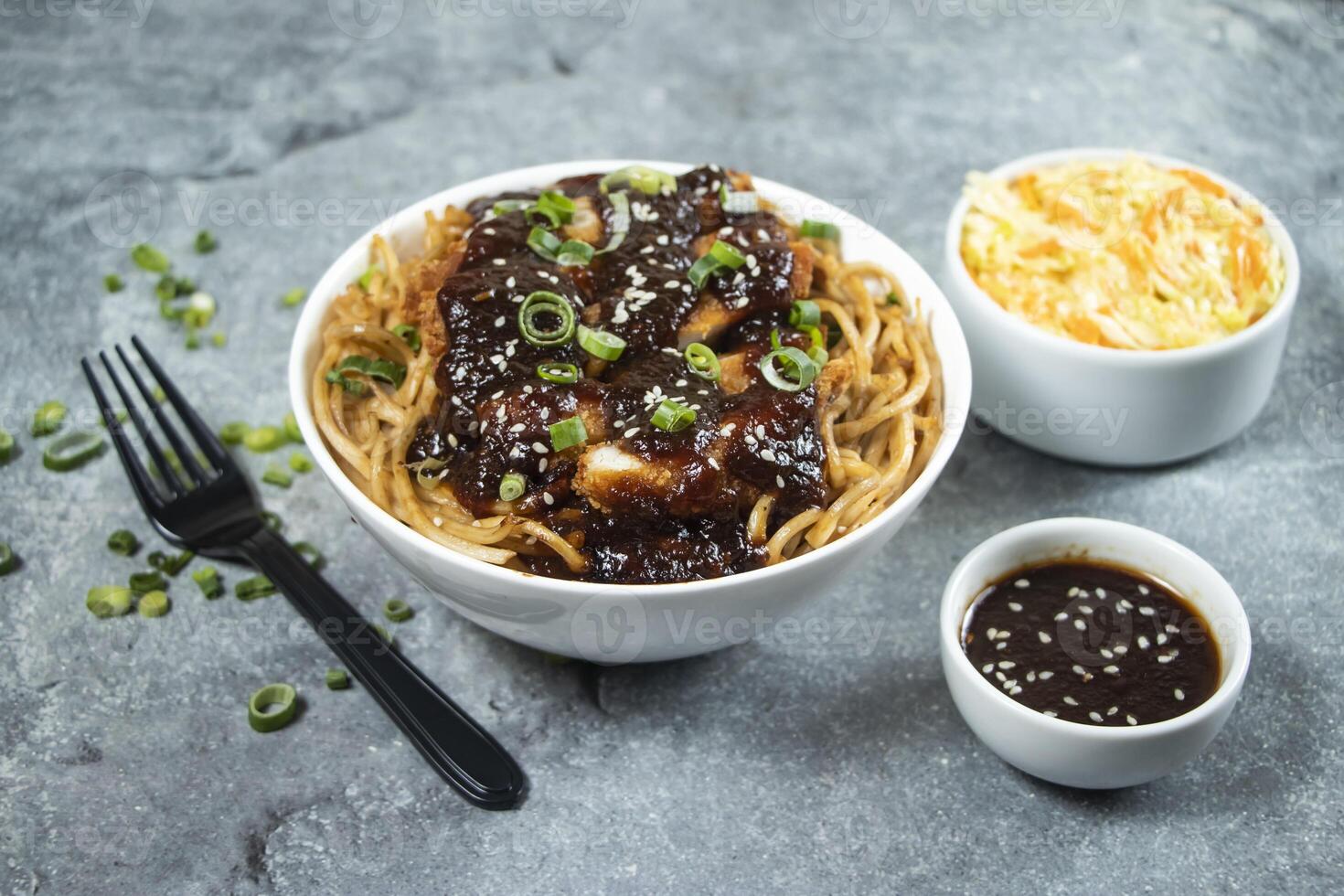 Teriyaki Fried Chicken Noodles with green onion, spicy sauce, cabbage salad and fork served in bowl isolated on grey background side view of asian food photo