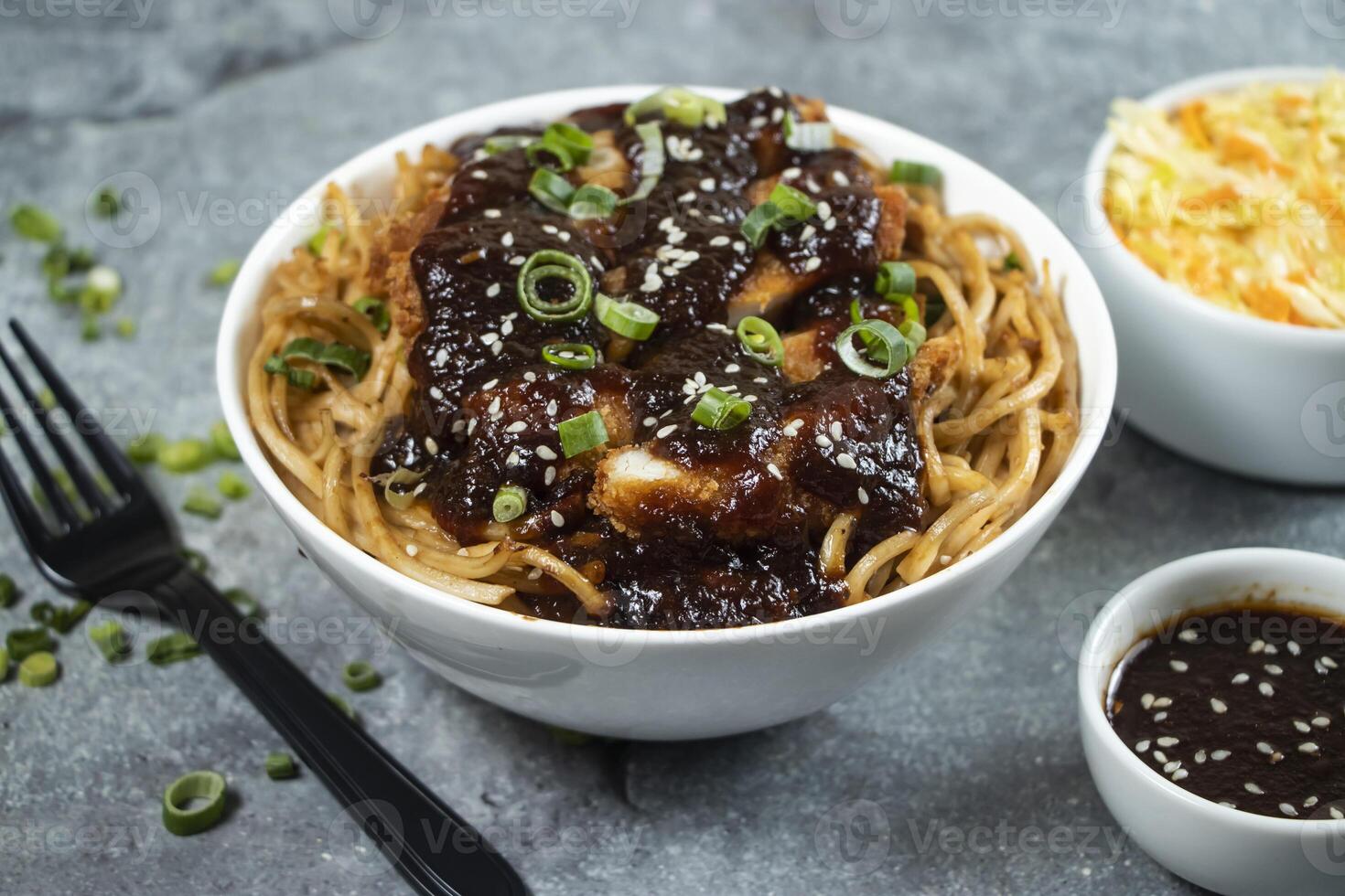 Teriyaki Fried Chicken Noodles with green onion, spicy sauce, cabbage salad and fork served in bowl isolated on grey background closeup side view of asian food photo
