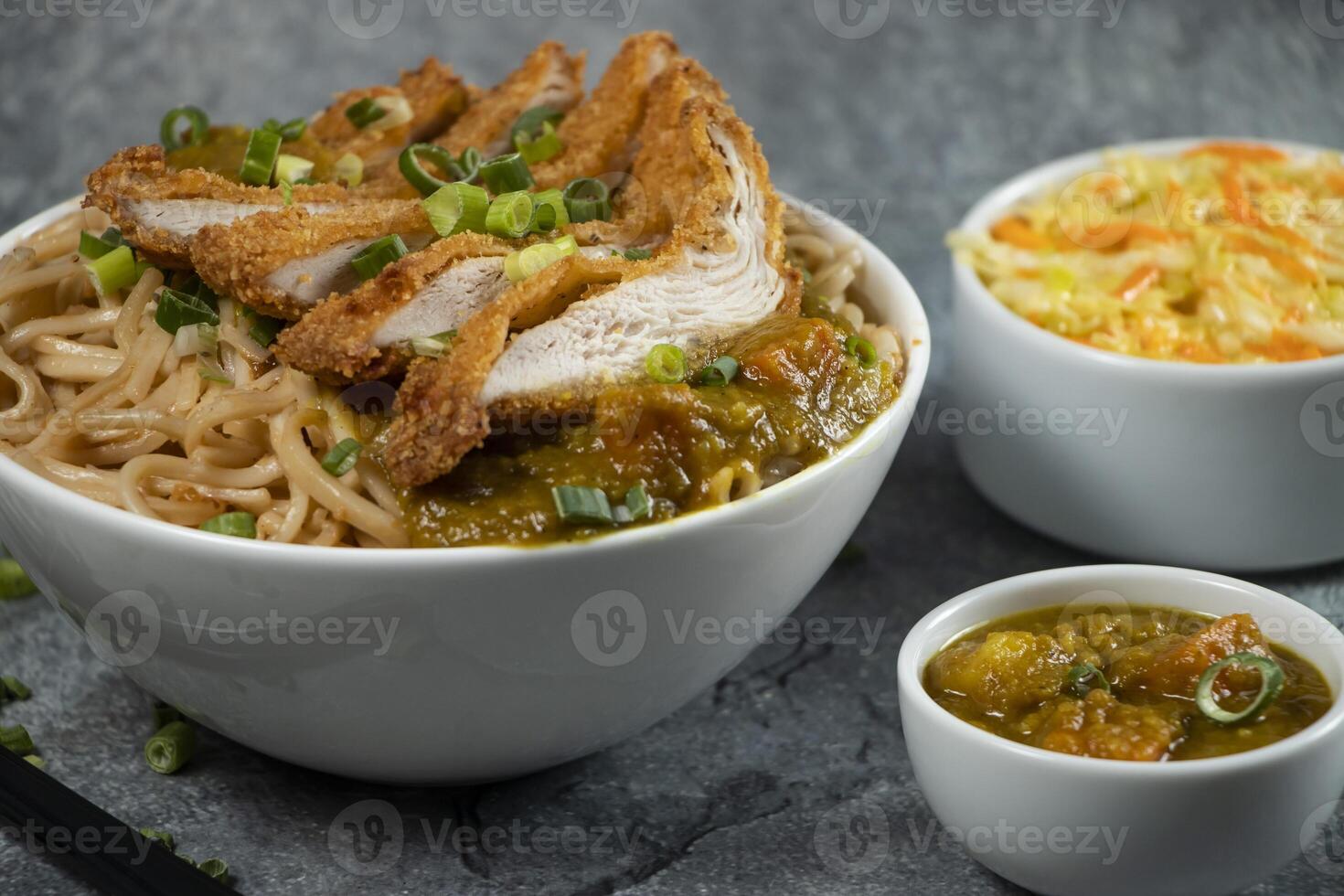 Katsu Chicken Noodles with potato curry, cabbage salad, green onion and fork served in bowl isolated on grey background closeup side view of Japanese food photo