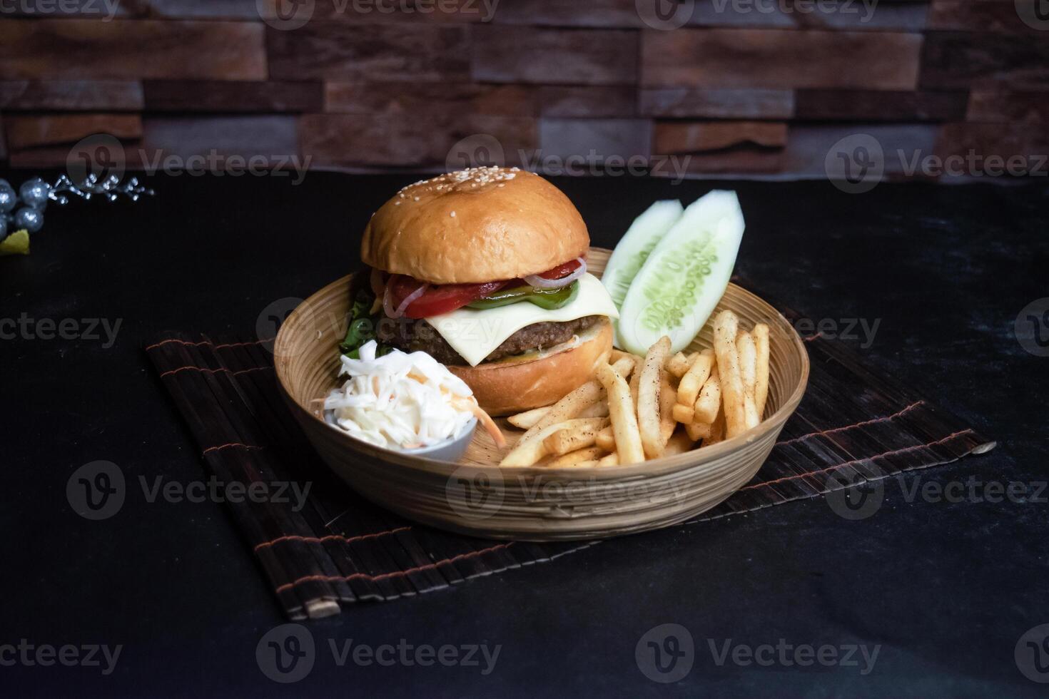 Beef cheese burger basket include tomato, onion, lettuce leave, capsicum, french fries and salad served in wooden plate isolated on dark background side view of bangladeshi fast food photo