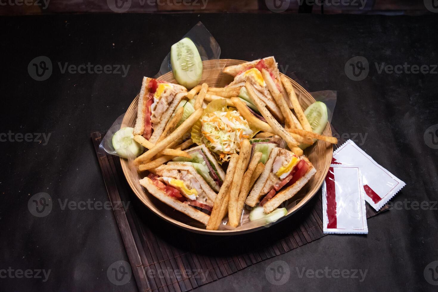 ultimate club sandwich with french fries and sauce served in basket isolated on dark background side view of bangladeshi fast food photo