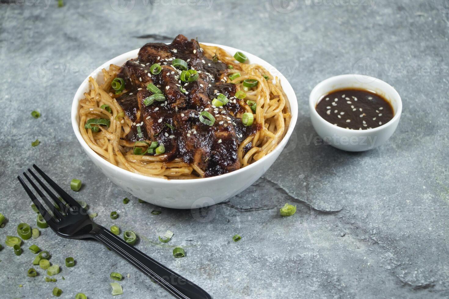 Teriyaki Grilled Chicken Noodles with green onion, spicy sauce and fork served in bowl isolated on grey background side view of asian food photo