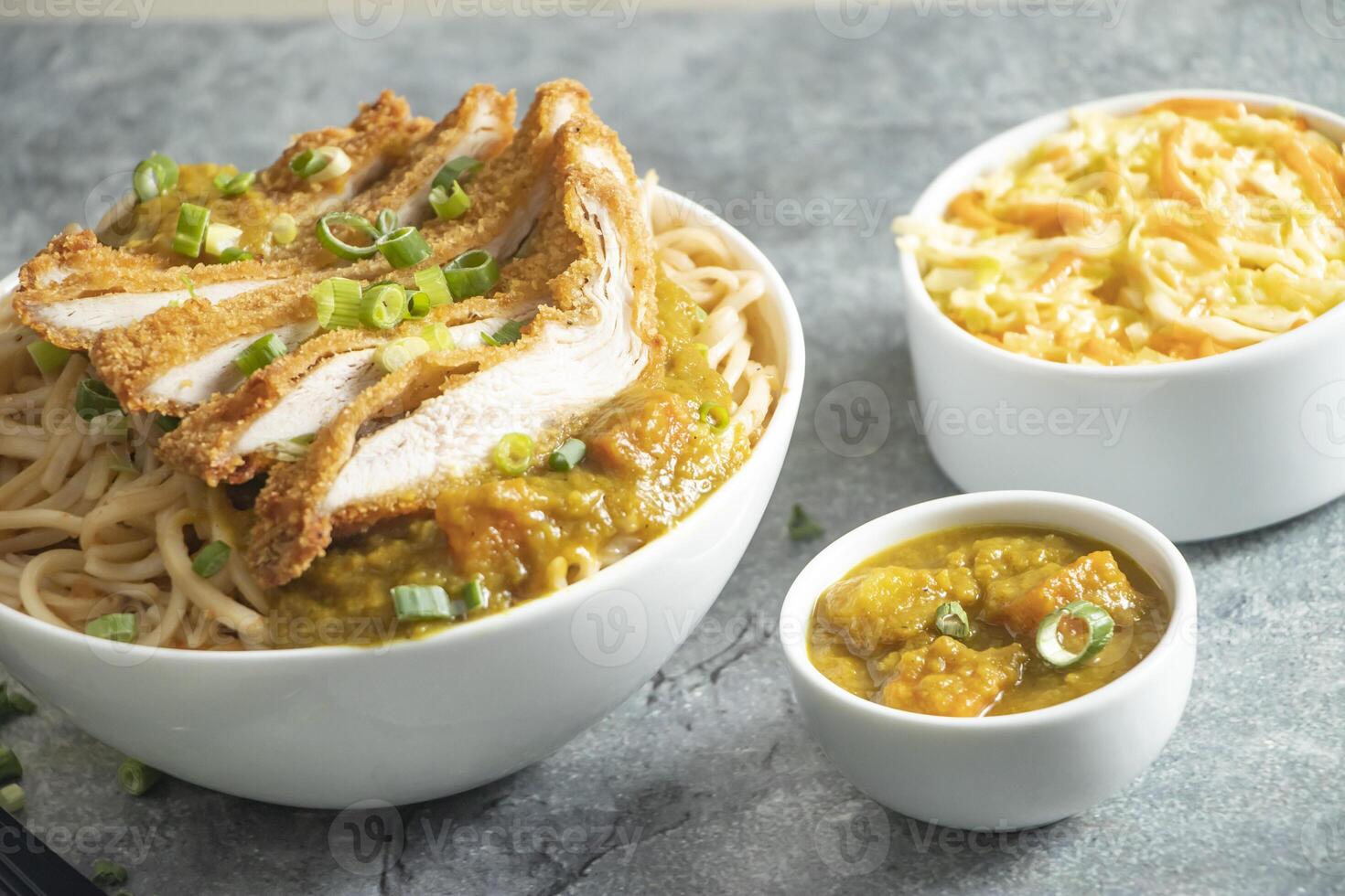 Katsu Chicken Noodles with potato curry, cabbage salad, green onion and fork served in bowl isolated on grey background closeup side view of japan food photo