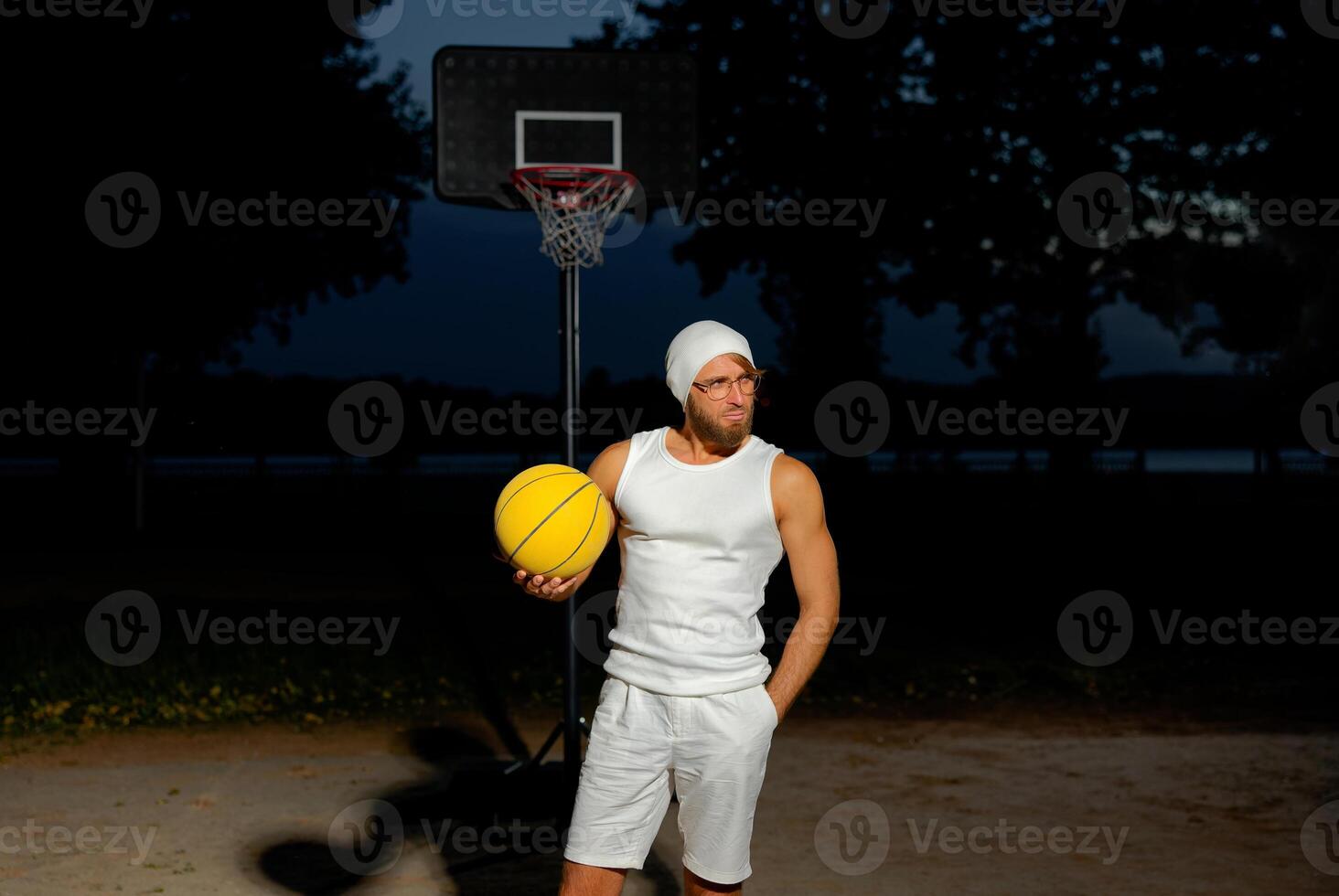 Man holding a basketball in a park at dusk, showcasing athleticism and confidence by the court under a darkening sky photo