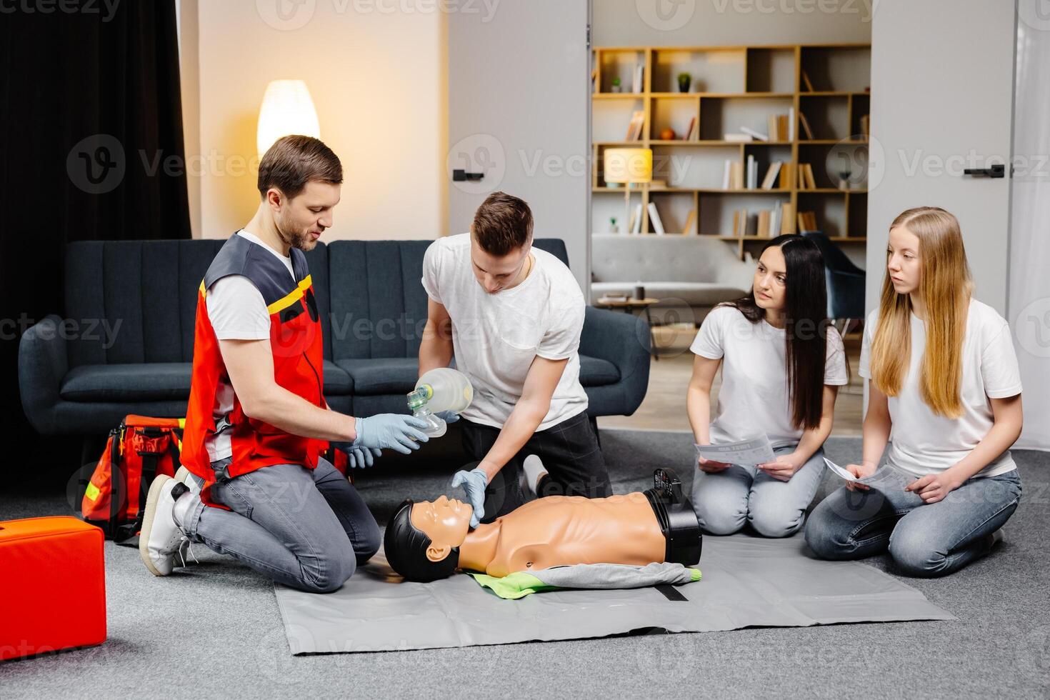 Young man instructor helping to make first aid heart compressions with dummy during the group training indoors photo