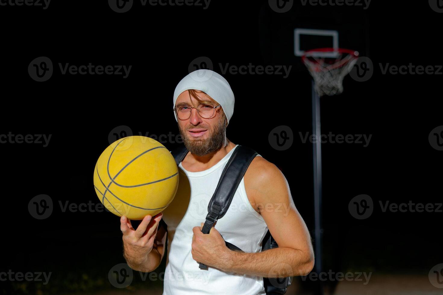 A man prepares for a night basketball game with a yellow ball at an outdoor court under dim lighting photo