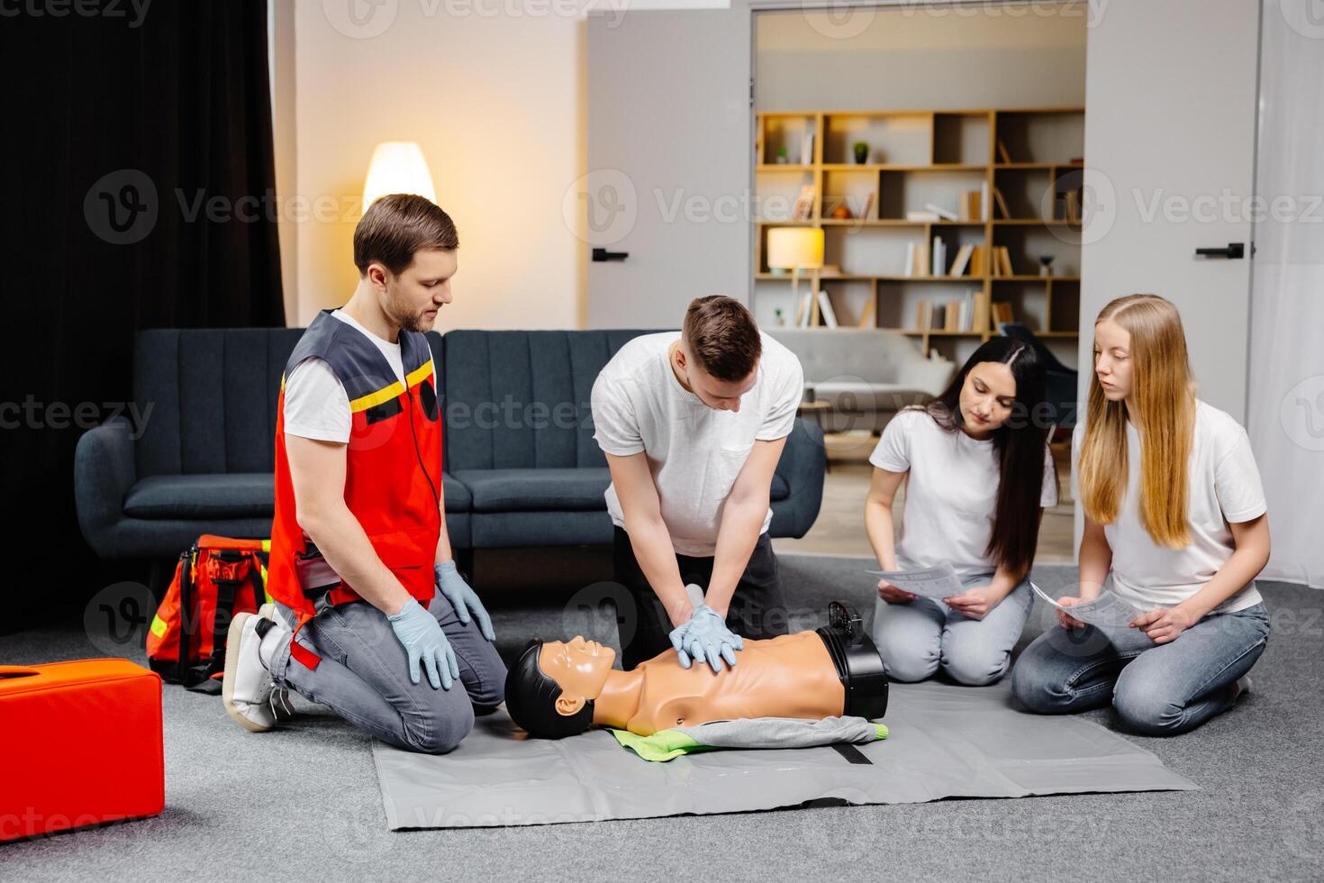 Young man instructor helping to make first aid heart compressions with dummy during the group training indoors photo