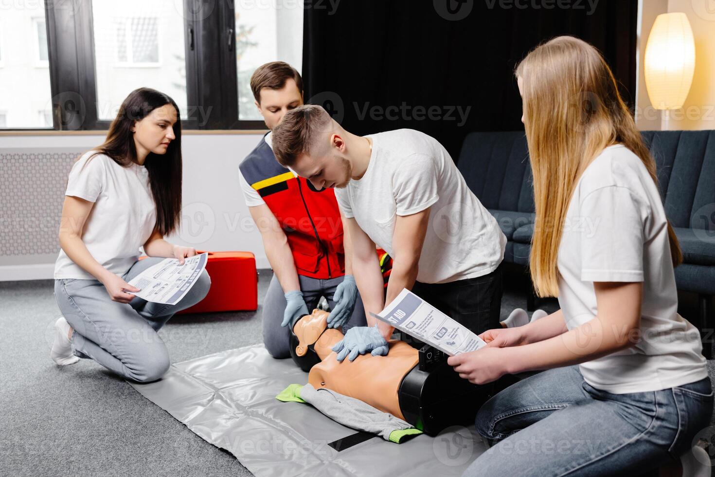 Young man instructor helping to make first aid heart compressions with dummy during the group training indoors photo