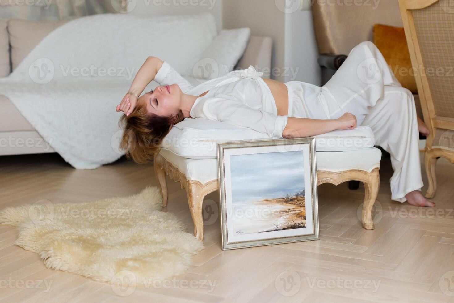 A woman is lying on a sofa in a stylish, bright living room next to a beautiful picture she painted herself. photo