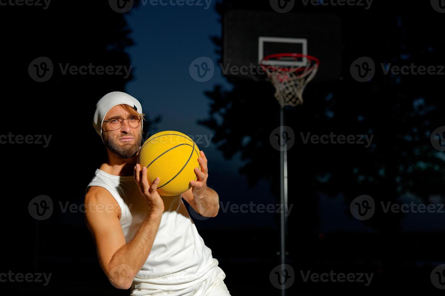 Man holding a basketball in a park at dusk, showcasing athleticism and confidence by the court photo
