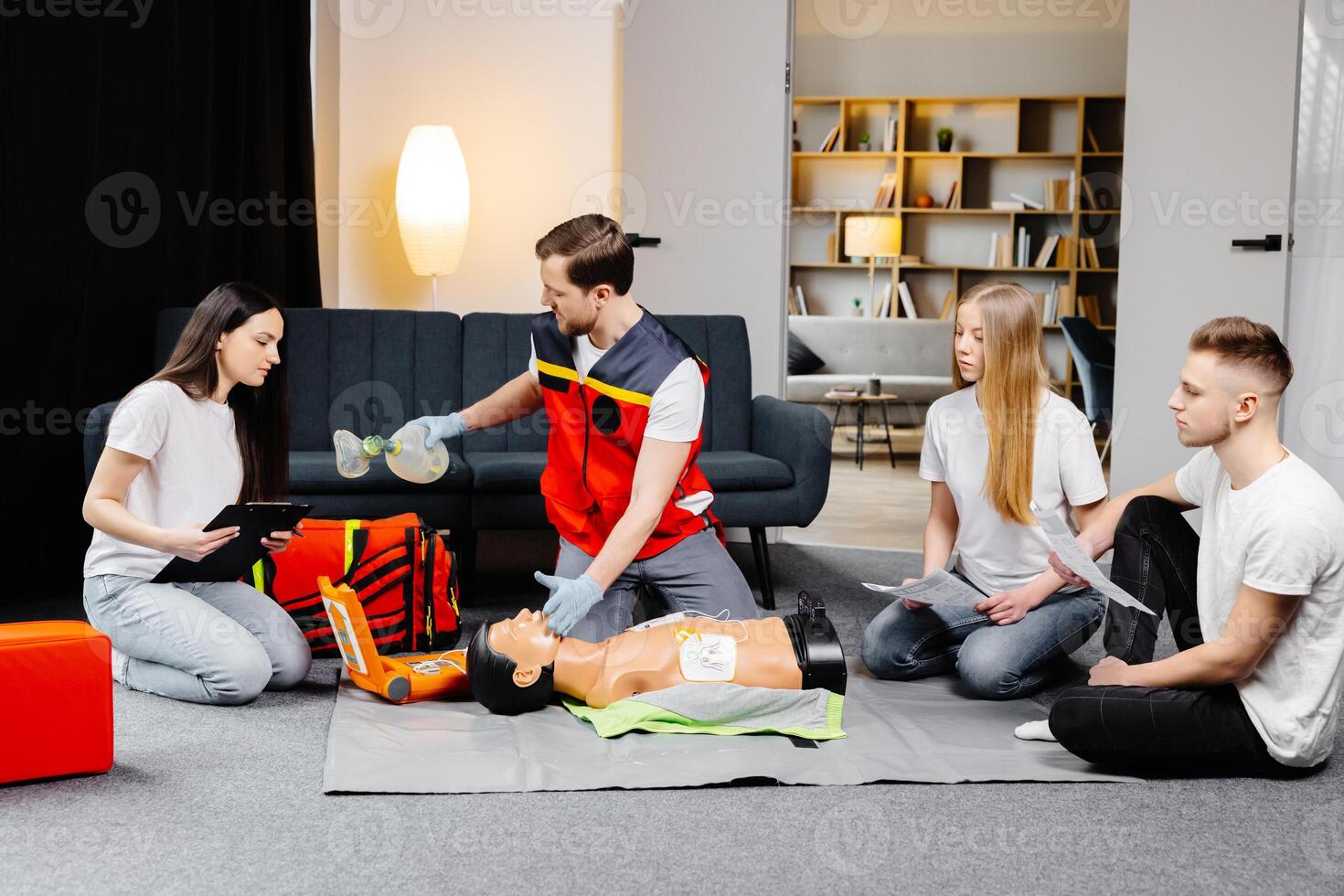 Young man instructor helping to make first aid heart compressions with dummy during the group training indoors photo