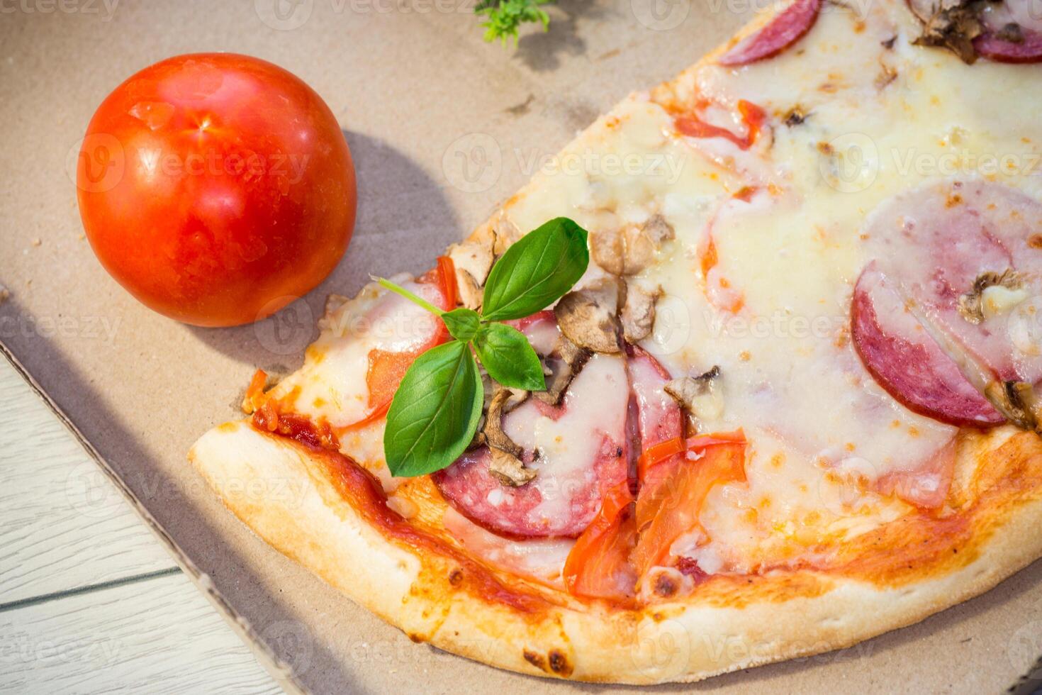 cooked pizza with salami and sausage in a box on a wooden table.On a wooden table photo