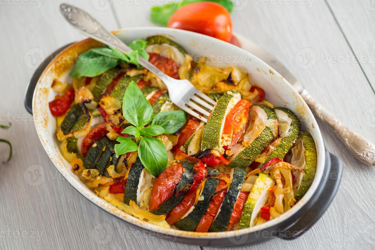 prepared baked zucchini and tomatoes in circles in a ceramic form. On a wooden table photo