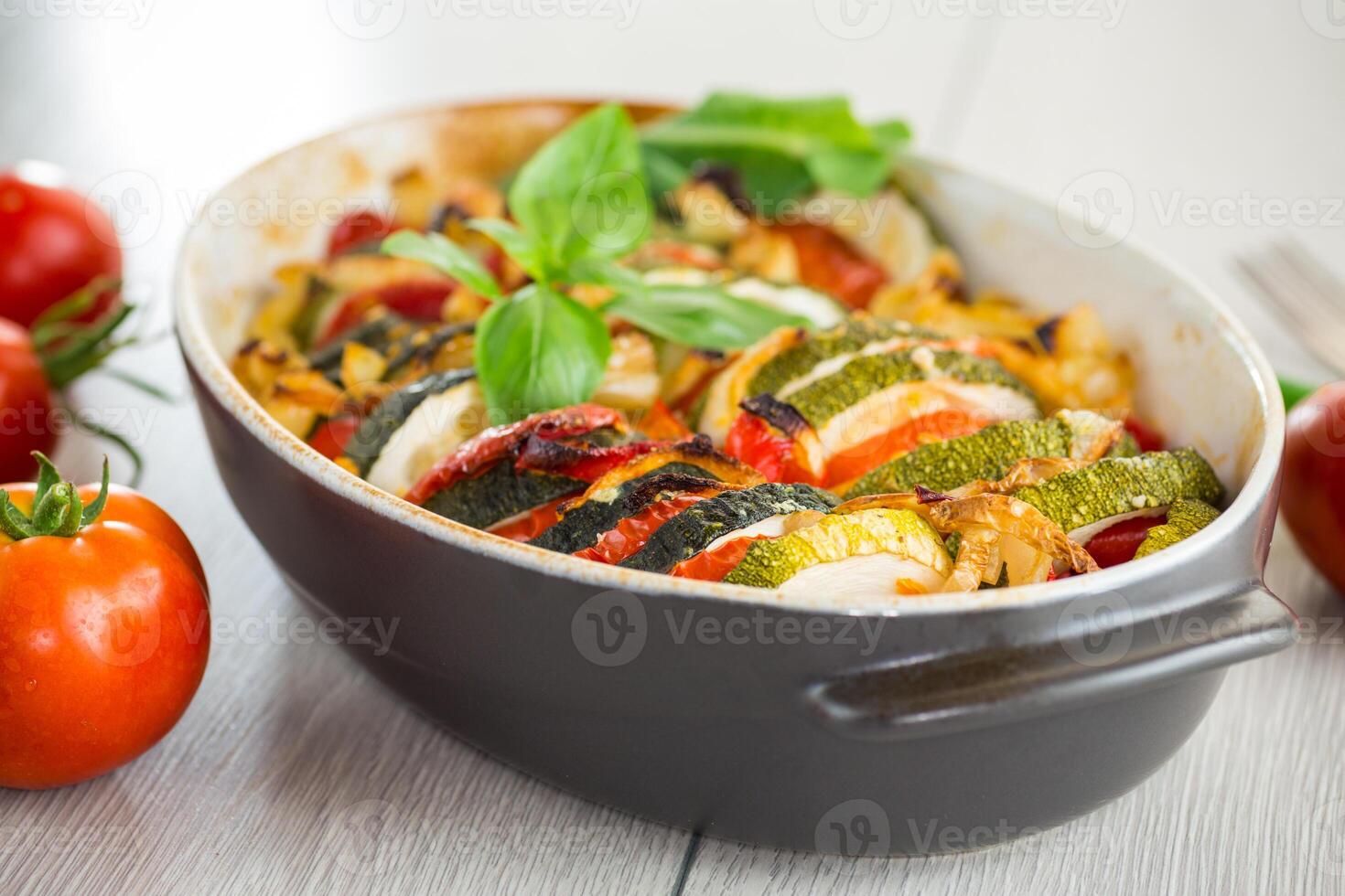 prepared baked zucchini and tomatoes in circles in a ceramic form, vegetable snack. On a wooden table photo