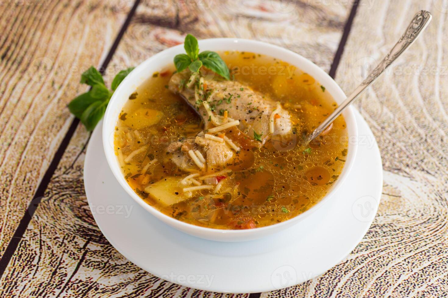 hot cooked chicken and noodle soup in a plate on a wooden table photo