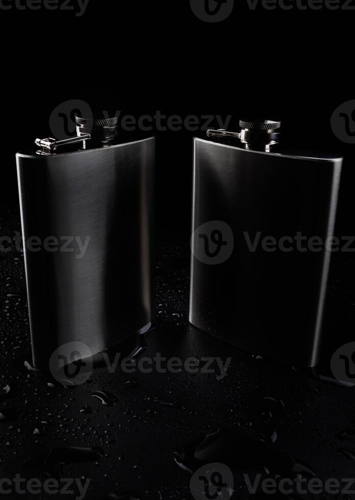 Two stainless steel flasks on a black background with water drops. photo