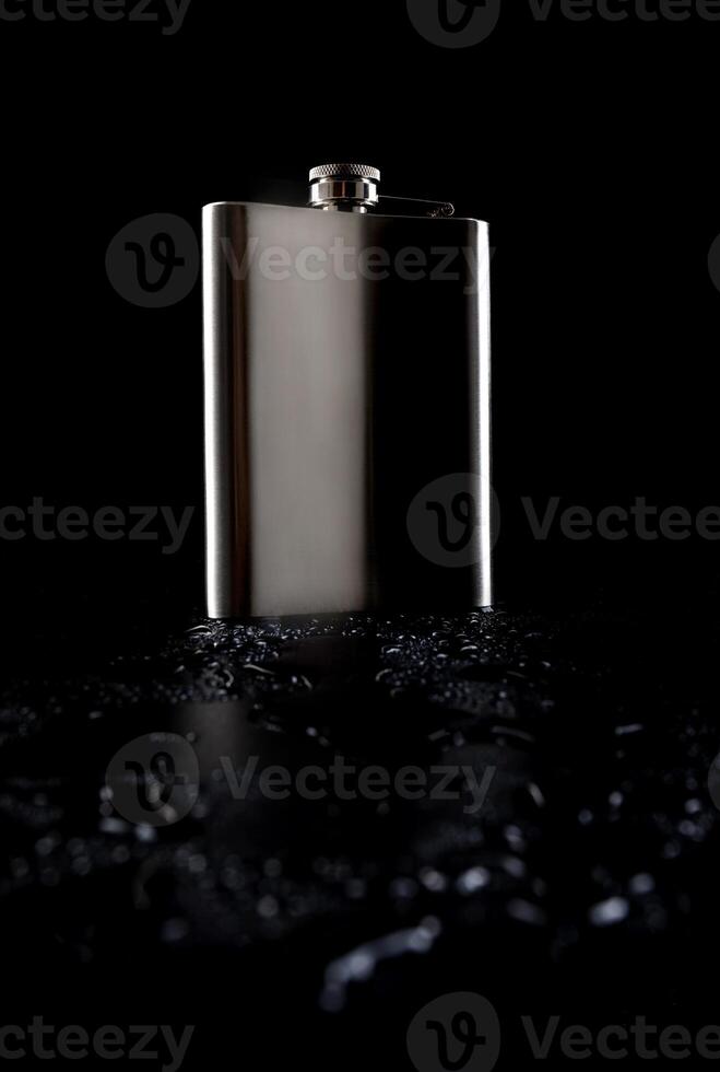 Flat stainless steel flask on a black background with water drops. photo