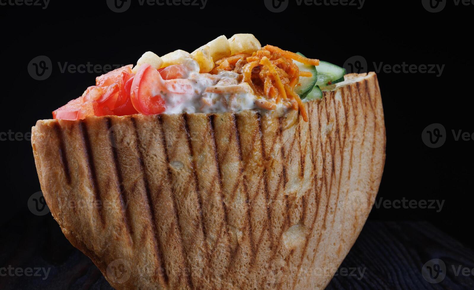 Doner with a crispy crust and delicious meat and vegetable filling on a dark background. photo