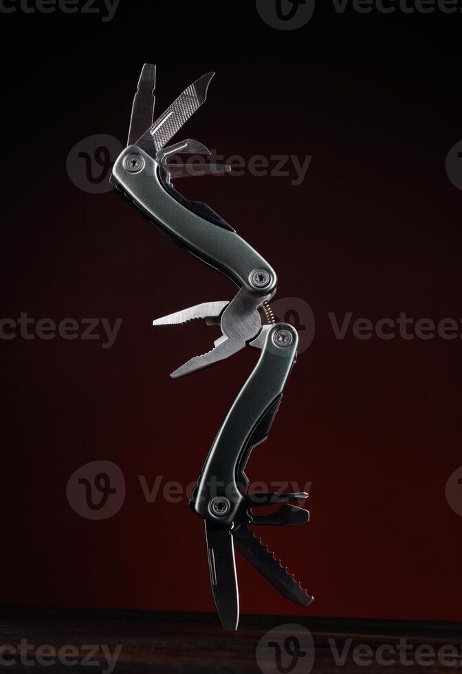 Steel open multitool on red background. Multitool with many useful tools. photo